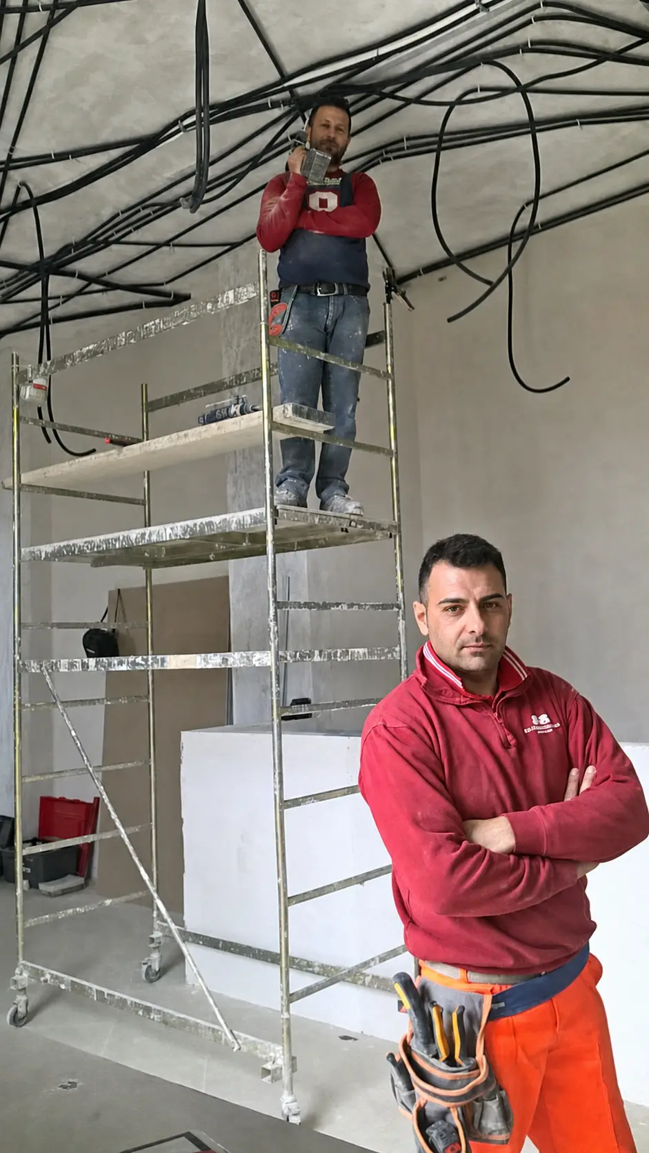 Francesco in un ambiente interno durante i lavori, davanti a un ponteggio e agli impianti in posa